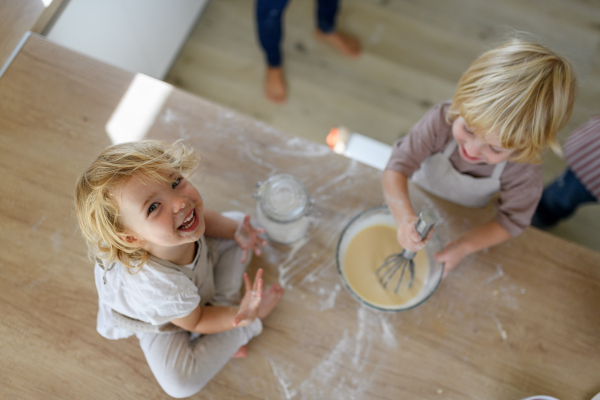 Little cute girl sitting on kitchen countertop, tasting pancake batter with finger. Nuclear family spending weekend day indoors, cooking together.