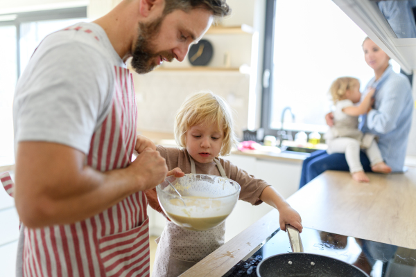 Nuclear family making pancakes together. Parents and children in kitchen, preparing pancake batter, spending weekend day indoors.