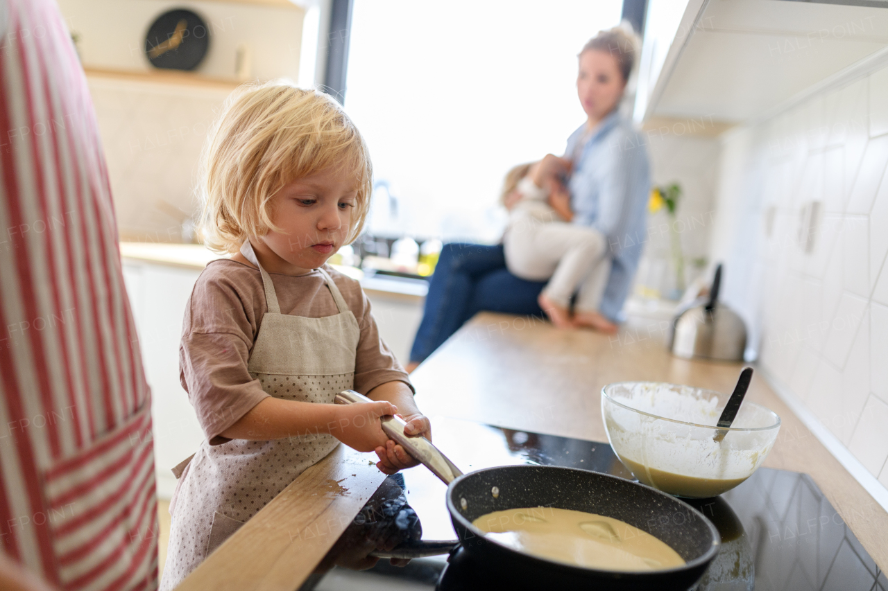 Young boy learning how to make pancakes, standing by stove. Parents and children in kitchen, preparing pancake batter, spending weekend day indoors