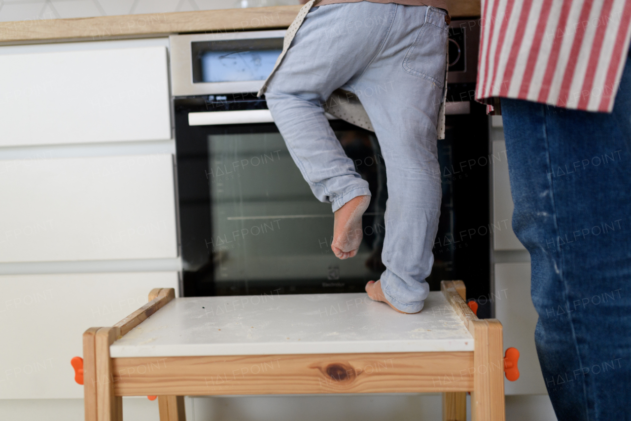 Boy learning how to make pancakes, standing on chair by stove. Parents and children in kitchen, preparing pancake batter, spending weekend day indoors