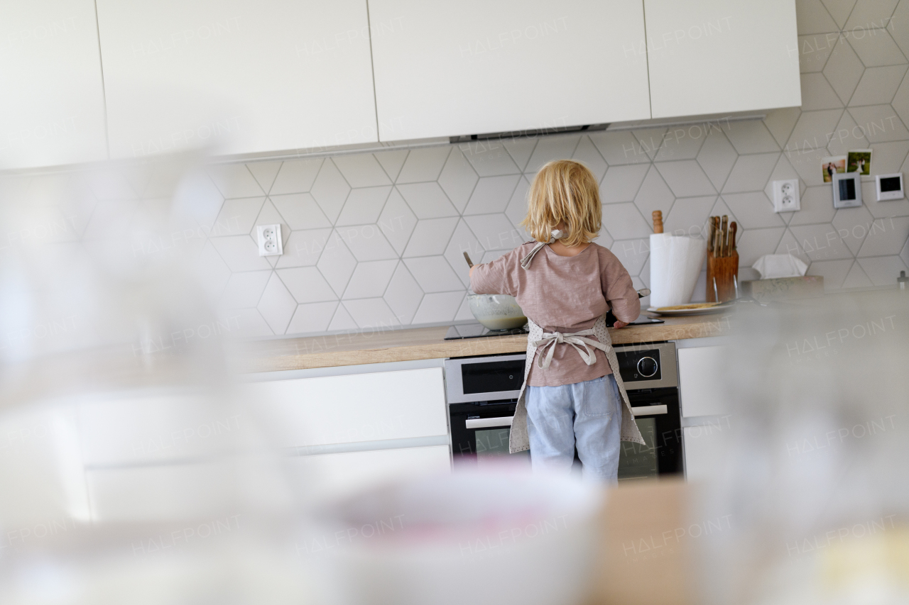 Young boy learning how to make pancakes, standing by stove. Parents and children in kitchen, preparing pancake batter, spending weekend day indoors