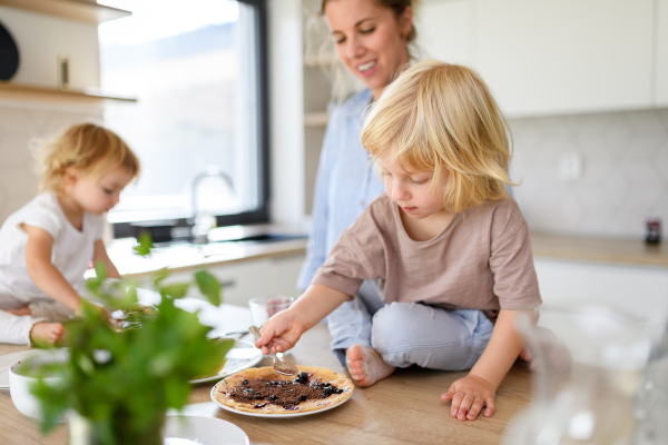 Family eating pancakes together, morning in kitchen. Mom and children spending weekend day indoors.