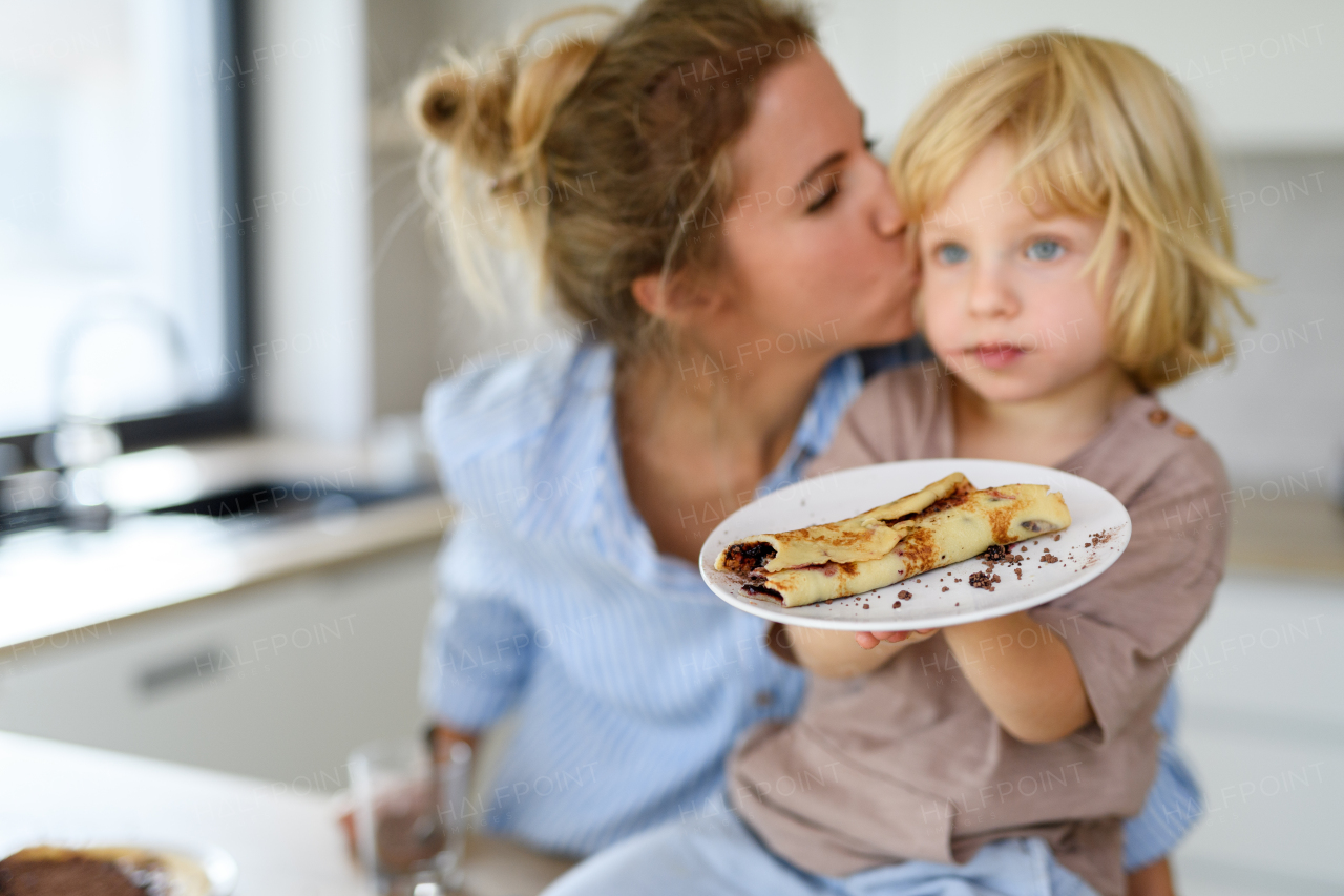 Mom and boy eating pancakes together, morning in kitchen for single mother. Parents and children spending weekend day indoors.