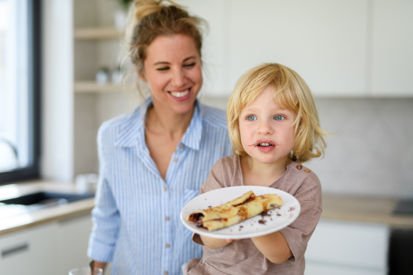 Mom and boy eating pancakes together, morning in kitchen for single mother. Parents and children spending weekend day indoors.