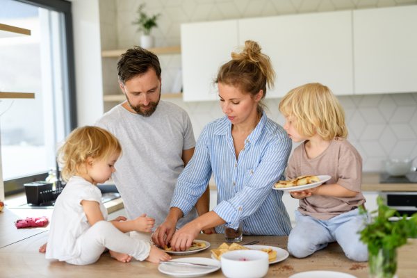 Family eating pancakes together, morning in kitchen. Parents and children spending weekend day indoors.