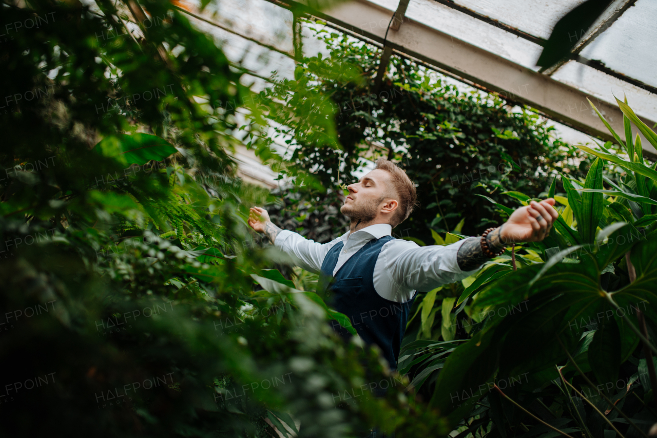 businessman standing in botanical garden, in the middle of lush green foliage, arms open. Concept of corporate social responsibility and ESG.