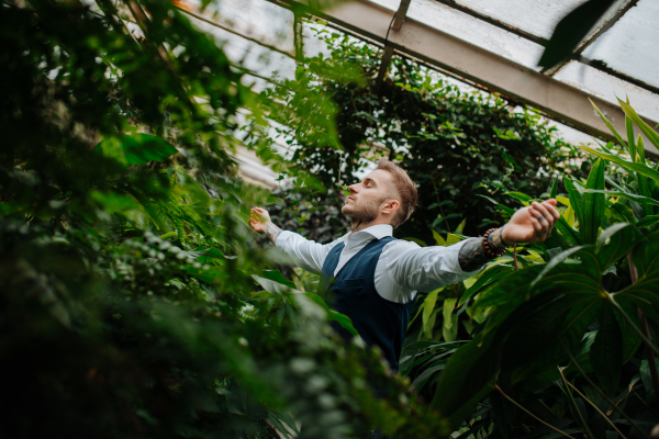 businessman standing in botanical garden, in the middle of lush green foliage, arms open. Concept of corporate social responsibility and ESG.