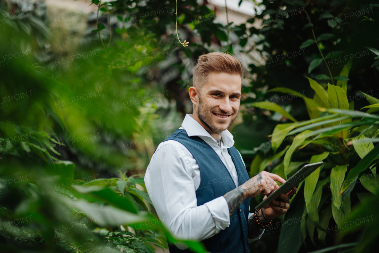 Businessman with tablet, standing in botanical garden, in the middle of lush green foliage. Concept of corporate social responsibility and ESG.