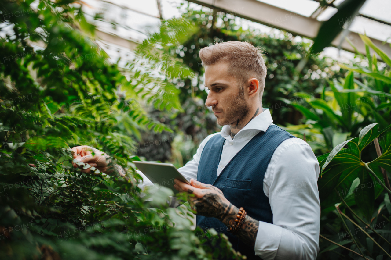 Businessman with tablet, standing in botanical garden, in the middle of lush green foliage, looking at camera. Concept of corporate social responsibility and ESG.