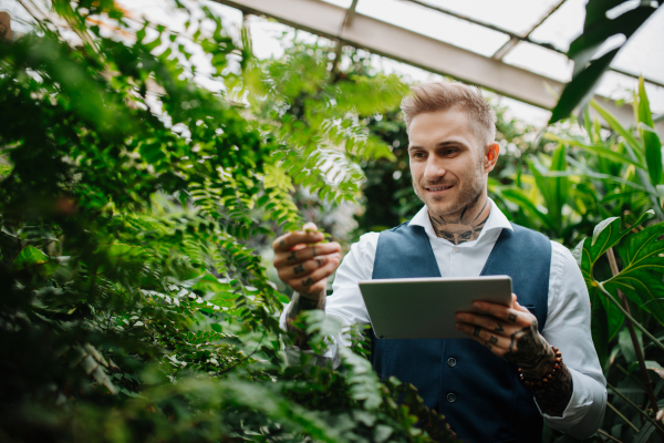 Businessman with tablet, standing in botanical garden, in the middle of lush green foliage. Concept of corporate social responsibility and ESG.