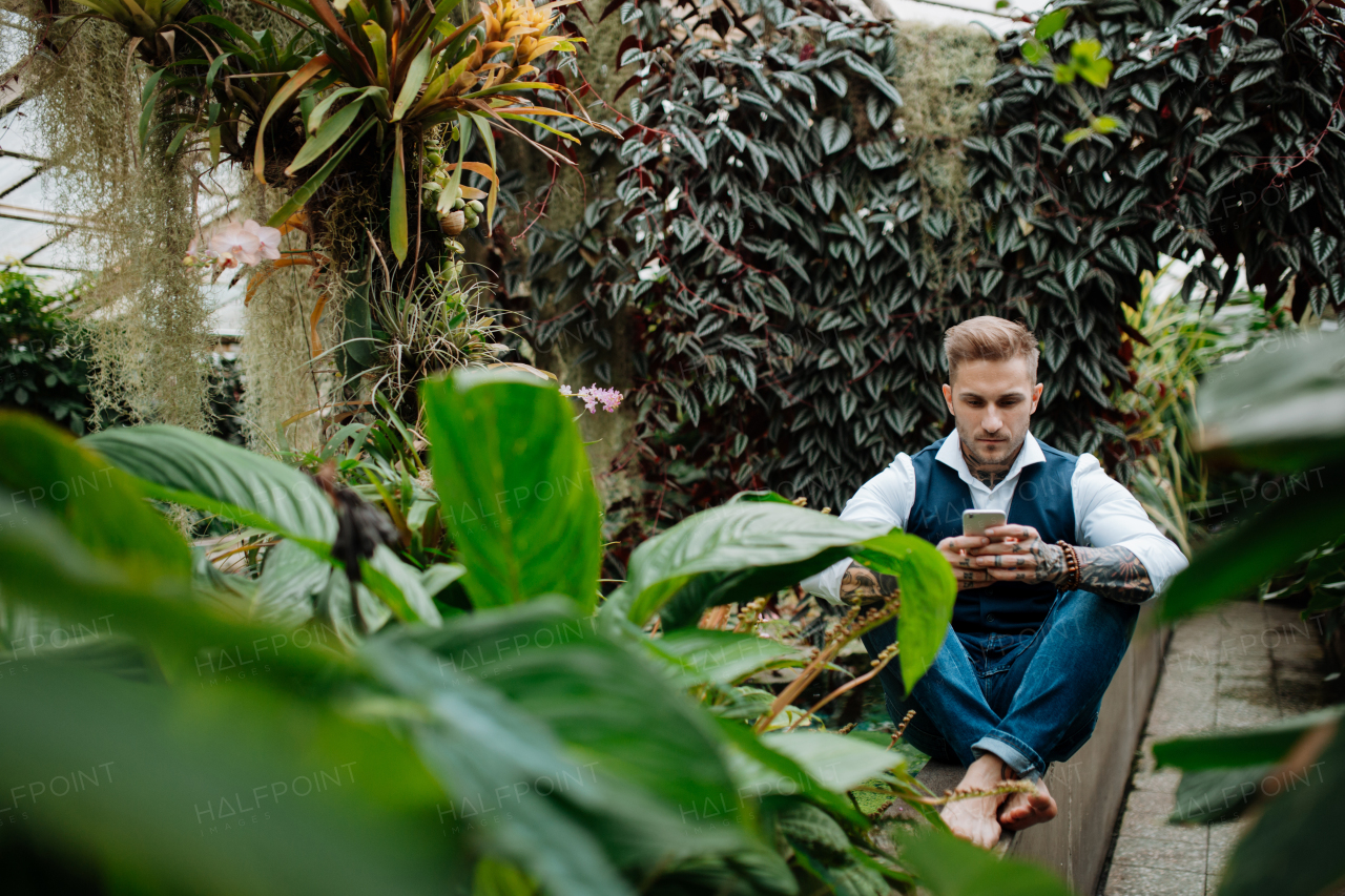 Businessman with smartphone, sitting in botanical garden, in the middle of lush green foliage.Concept of corporate social responsibility and ESG.