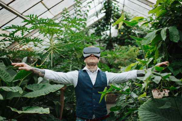 Businessman standing in botanical garden, in the middle of lush green foliage, using VR headset.