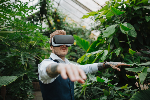 Businessman standing in botanical garden, in the middle of lush green foliage, using VR headset.