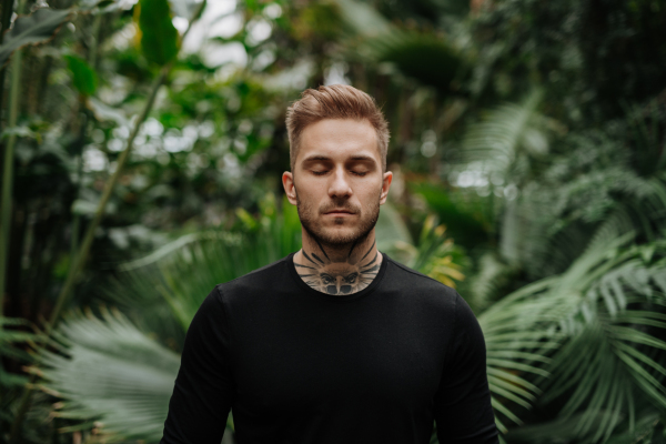 Handsome man with tattoo standing in botanical garden, in the middle of lush green foliage.