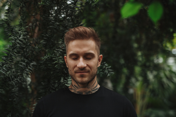 Handsome man with tattoo standing in botanical garden, in the middle of lush green foliage.