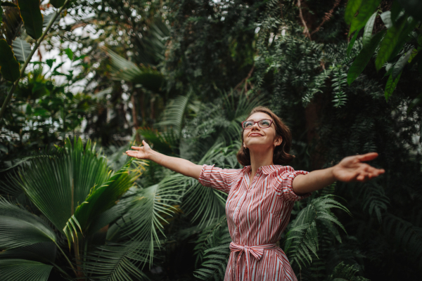 Woman standing in botanical garden, in the middle of lush green foliage, arms open.