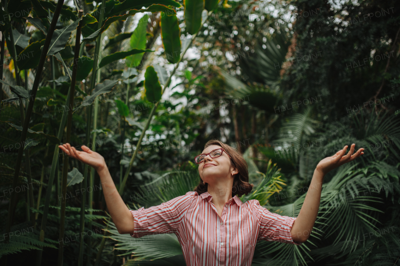 Woman standing in botanical garden, in the middle of lush green foliage, arms open.