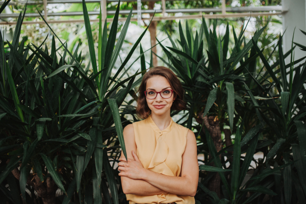 Businesswoman selling flowers and seedlings, standing in greenhouse, looking at camera, smiling. Small greenhouse business.