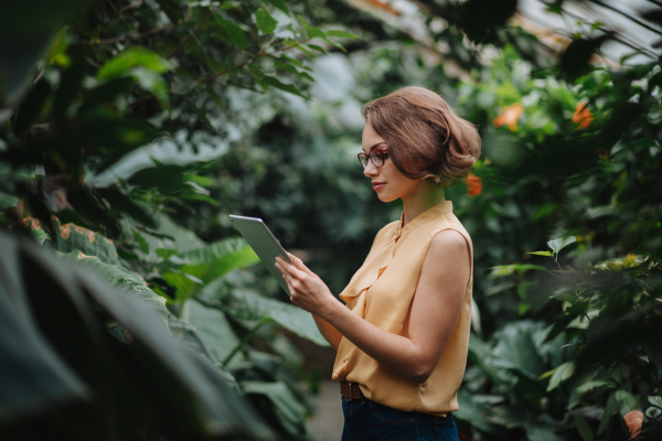 Businesswoman selling flowers and seedlings, standing in greenhouse, looking at camera, smiling. Small greenhouse business.