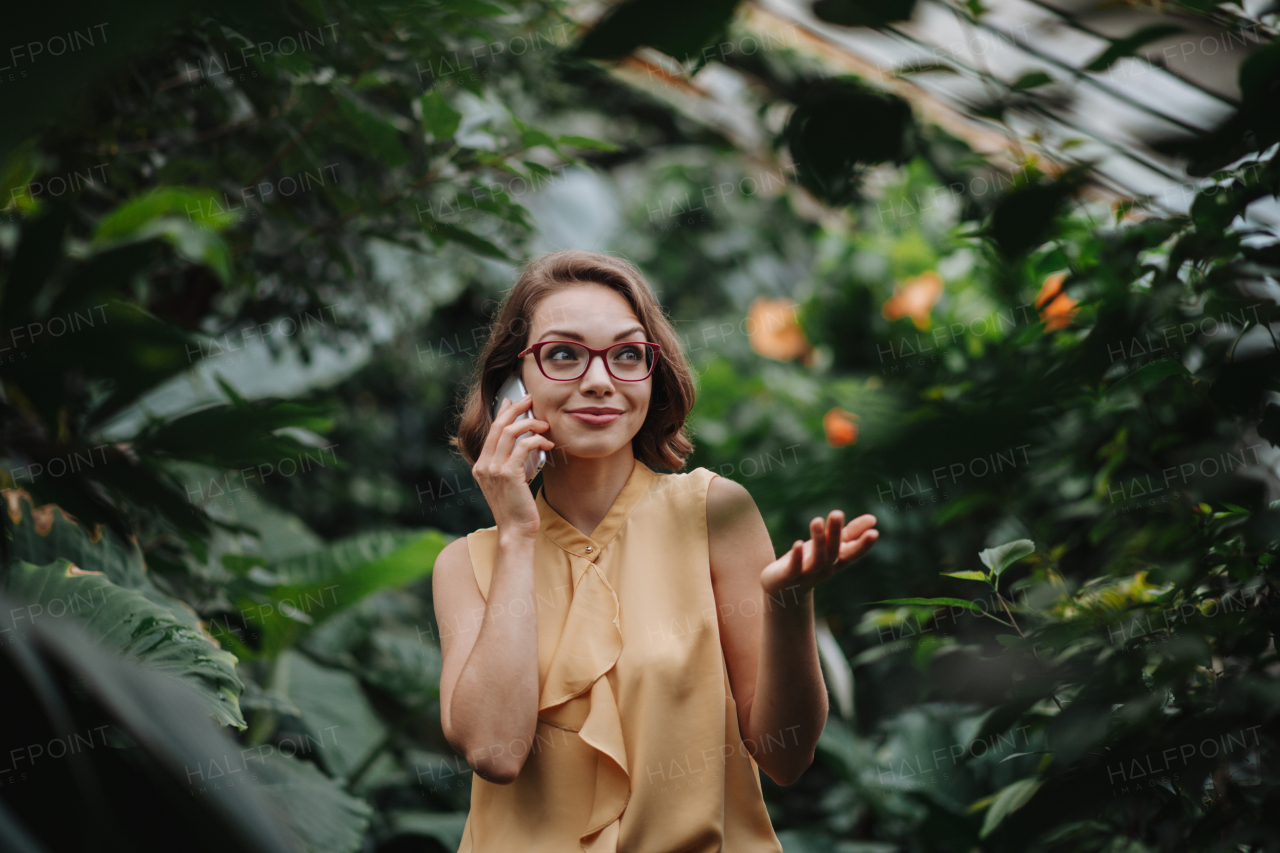 Small greenhouse business. Businesswoman selling flowers and houseplants, making phone call from greenhouse