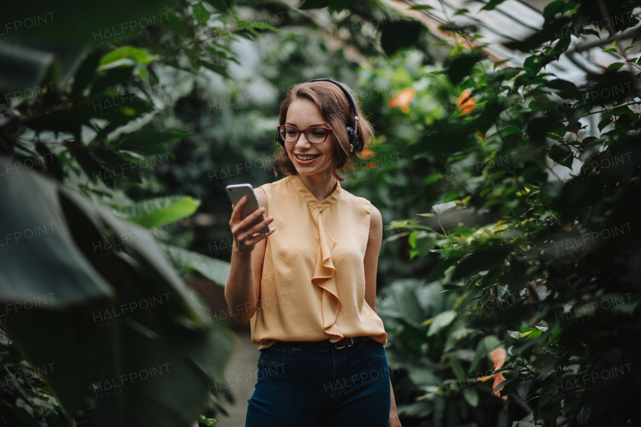 Businesswoman with smartphone standing in botanical garden, in the middle of lush green foliage, looking at camera. Concept of corporate social responsibility and ESG.