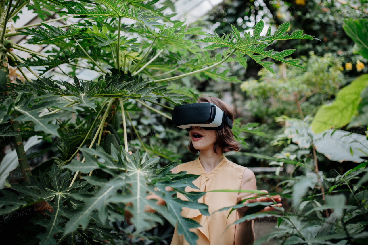 Businesswoman standing in botanical garden, in the middle of lush green foliage, using VR headset