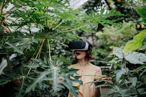 Businesswoman standing in botanical garden, in the middle of lush green foliage, using VR headset