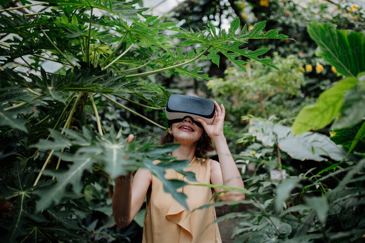 Businesswoman standing in botanical garden, in the middle of lush green foliage, using VR headset