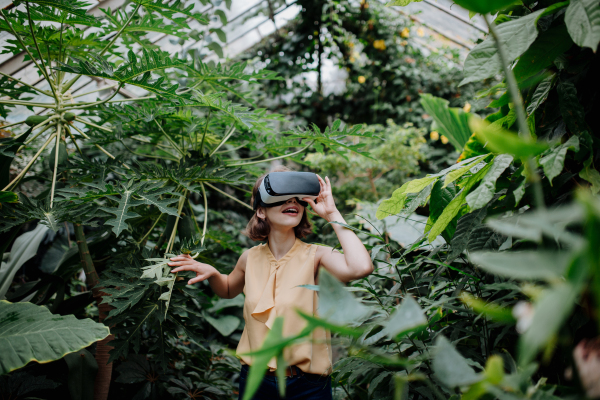 Businesswoman standing in botanical garden, in the middle of lush green foliage, using VR headset