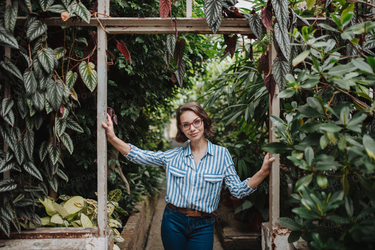 Businesswoman selling flowers and seedlings, standing in greenhouse, looking at camera, smiling. Small greenhouse business.