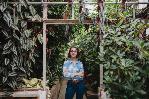 Businesswoman selling flowers and seedlings, standing in greenhouse, looking at camera, smiling. Small greenhouse business.