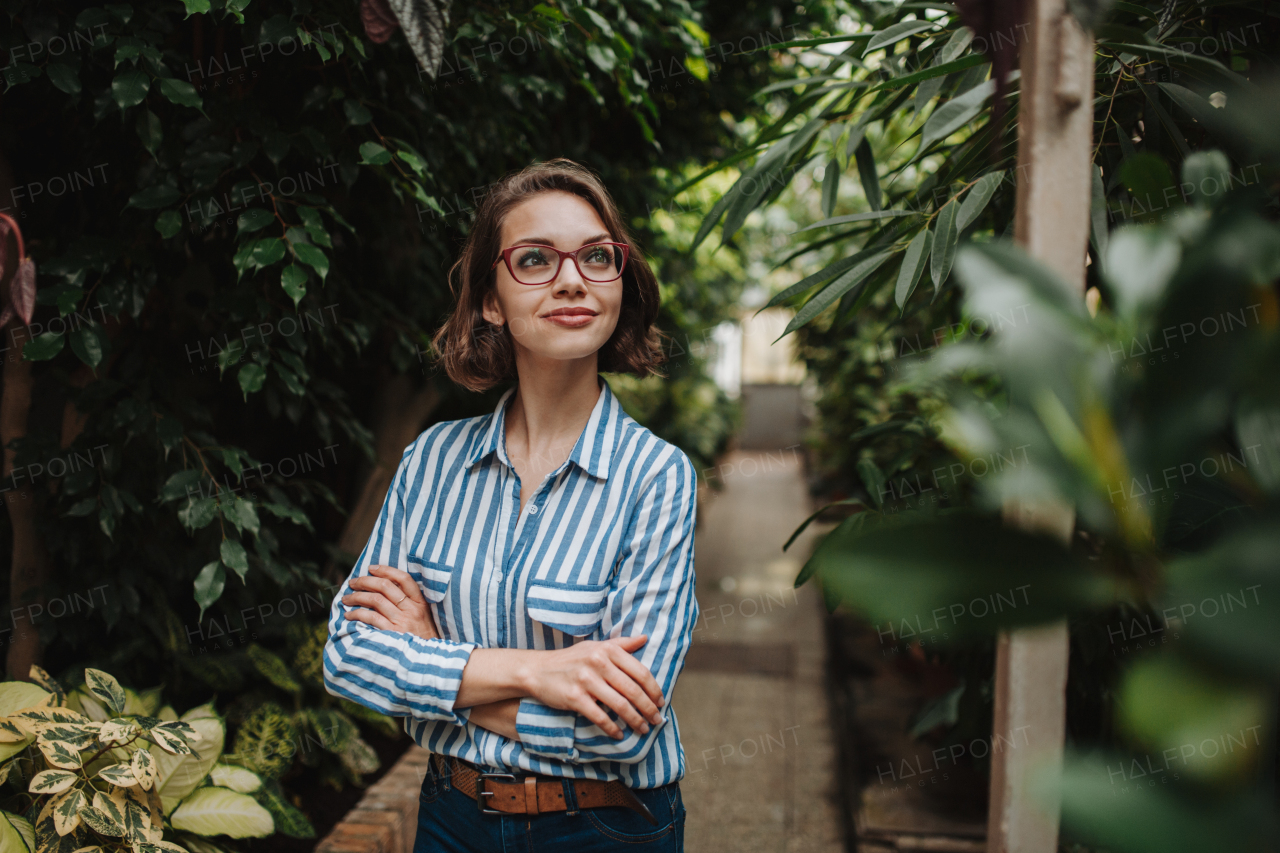 Businesswoman selling flowers and seedlings, standing in greenhouse, looking at camera, smiling. Small greenhouse business.