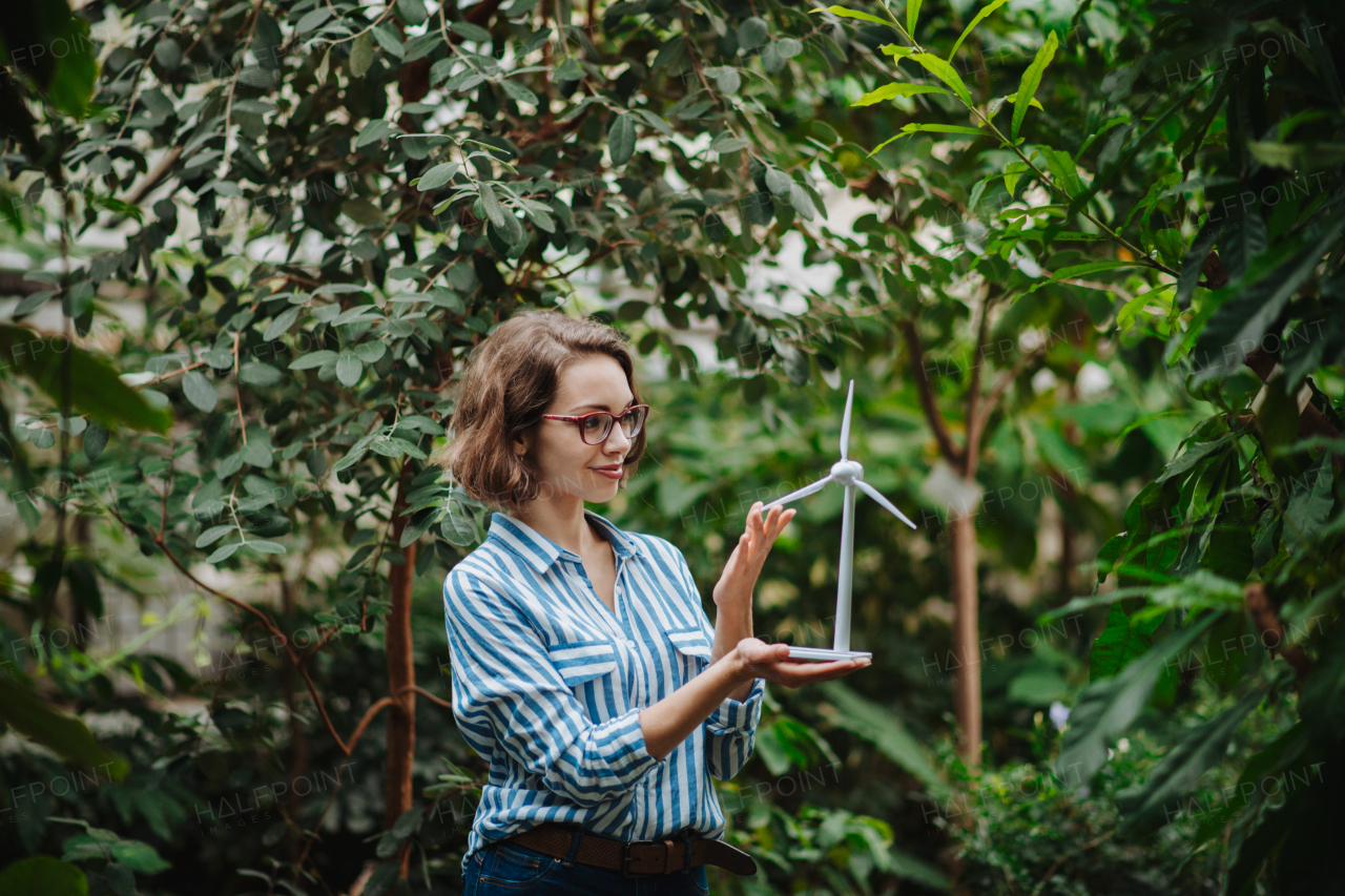 Woman standing in botanical garden, in the middle of lush green foliage, holding model of wind turbine.