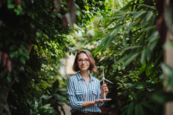 Woman standing in botanical garden, in the middle of lush green foliage, holding model of wind turbine.