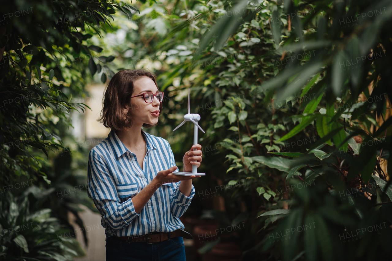 Woman standing in botanical garden, in the middle of lush green foliage, holding model of wind turbine.