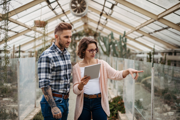 Businesswoman and manager talking, standing in greenhouse, looking at camera, smiling. Small greenhouse business.