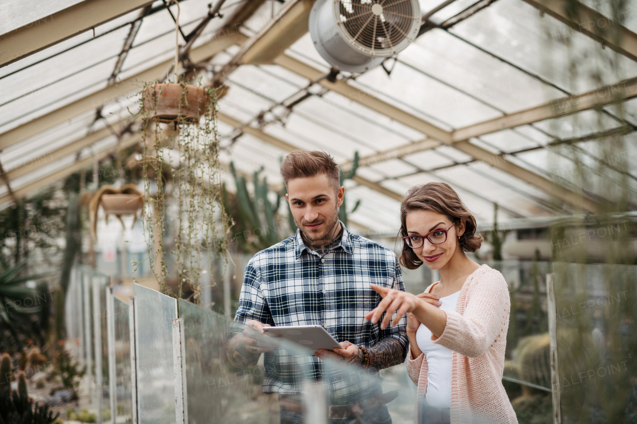 Businesswoman and manager talking, standing in greenhouse, looking at camera, smiling. Small greenhouse business.