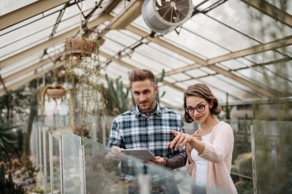 Businesswoman and manager talking, standing in greenhouse, looking at camera, smiling. Small greenhouse business.