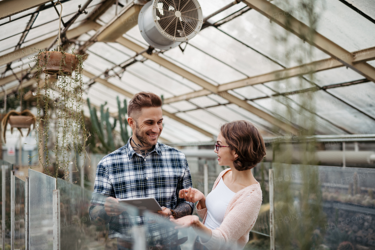 Businesswoman and manager talking, standing in greenhouse, looking at camera, smiling. Small greenhouse business.