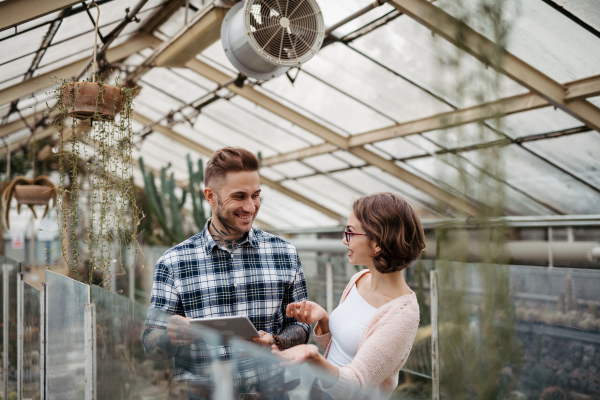 Businesswoman and manager talking, standing in greenhouse, looking at camera, smiling. Small greenhouse business.