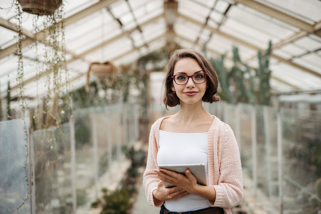 Businesswoman selling flowers and seedlings, standing in greenhouse, looking at camera, smiling. Small greenhouse business.