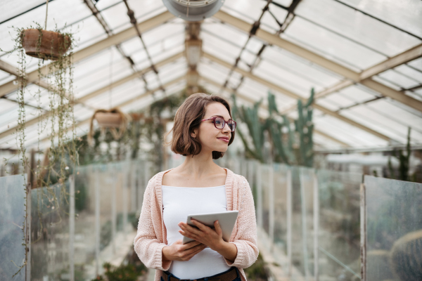 Businesswoman selling flowers and seedlings, standing in greenhouse, looking at camera, smiling. Small greenhouse business.