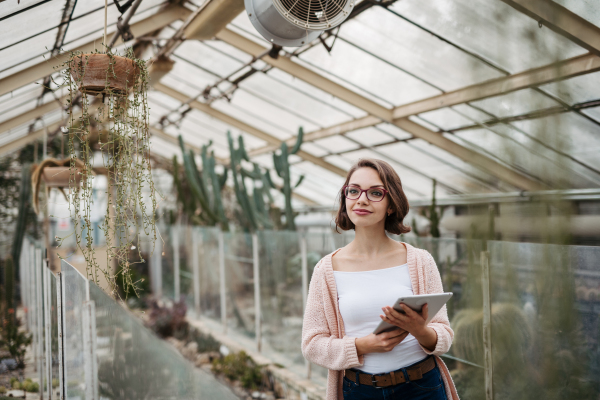 Businesswoman selling flowers and seedlings, standing in greenhouse, looking at camera, smiling. Small greenhouse business.