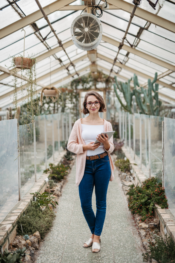 Businesswoman selling flowers and seedlings, standing in greenhouse, looking at camera, smiling. Small greenhouse business.