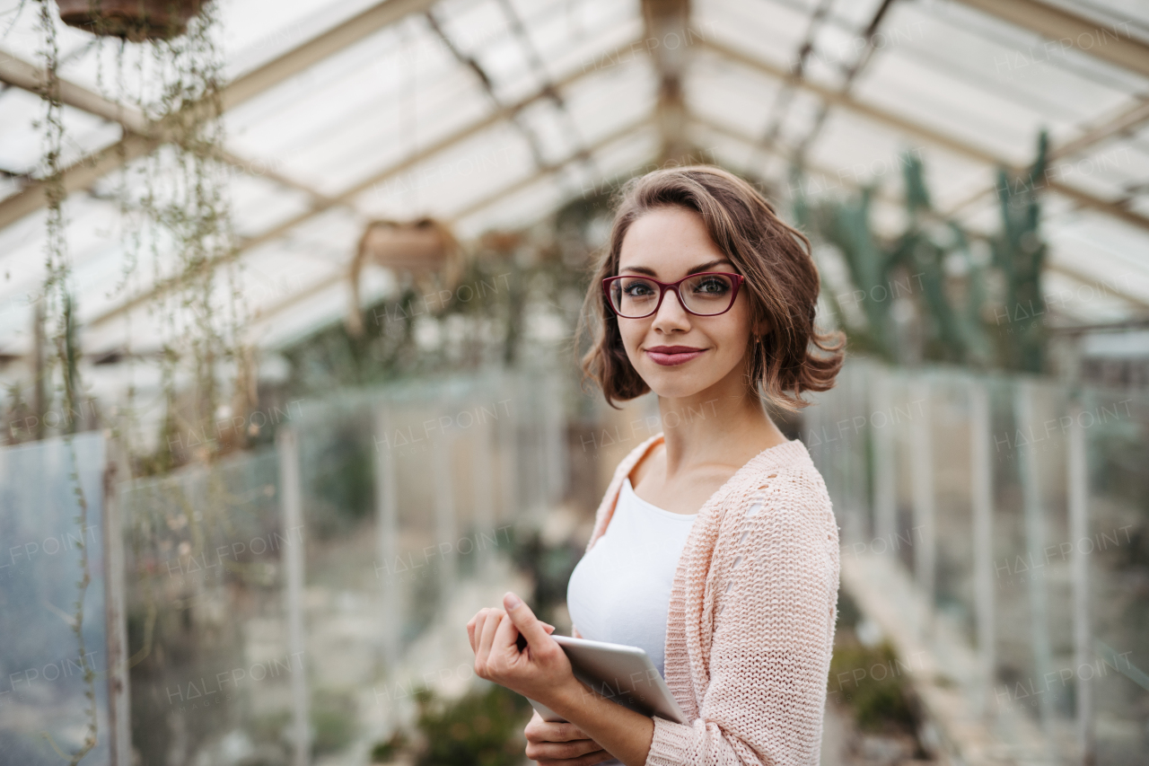 Businesswoman selling flowers and seedlings, standing in greenhouse, looking at camera, smiling. Small greenhouse business.