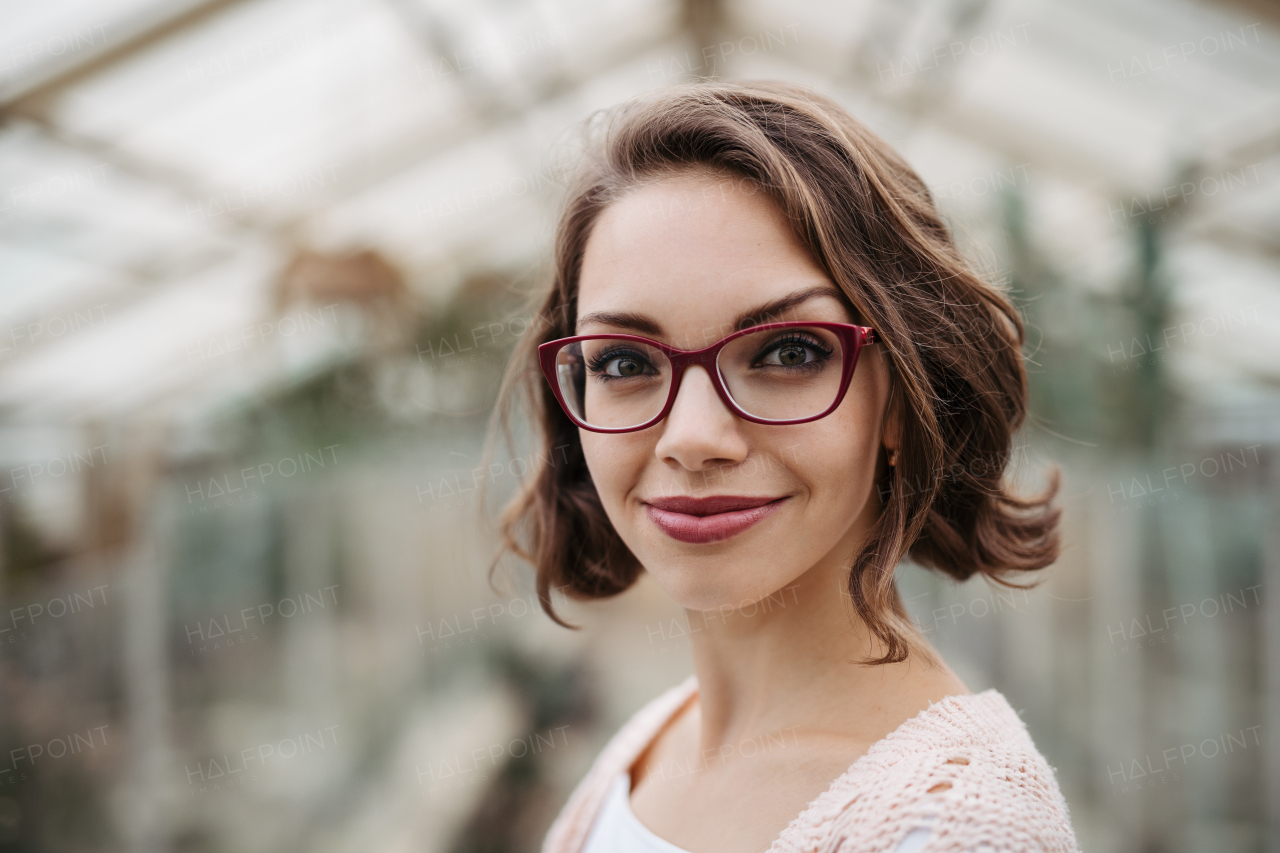 Businesswoman selling flowers and seedlings, standing in greenhouse, looking at camera, smiling. Small greenhouse business.