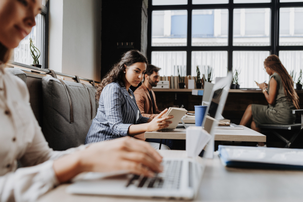 Group of freelancers and remote businesspeople working in shared work area. Concept of coworking, common workspaces for business, startups. Working remotely from coffee shop.