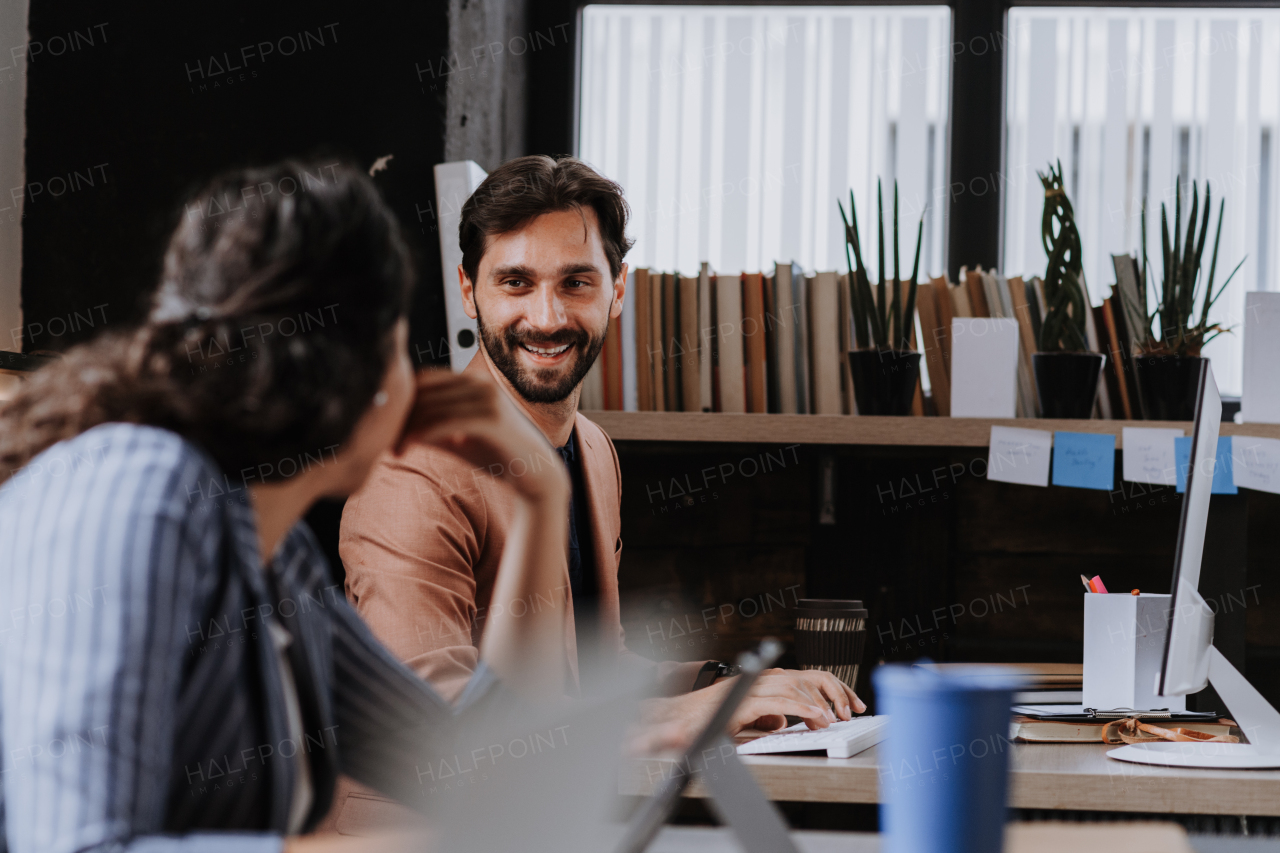 Two freelancers talking while working in shared work area. Concept of coworking, common workspaces for business, startups. Working remotely from coffee shop.