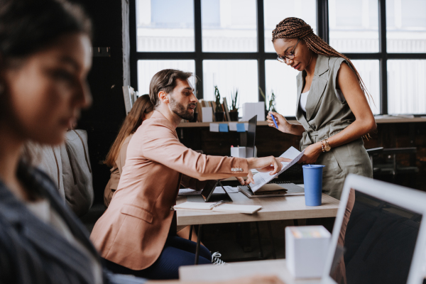 People in coworking space sharing ideas, collaboring, talking about project. Group of freelancers and remote businesspeople working in shared work area. Concept of coworking as modern working arragement. Working remotely from coffee shop.