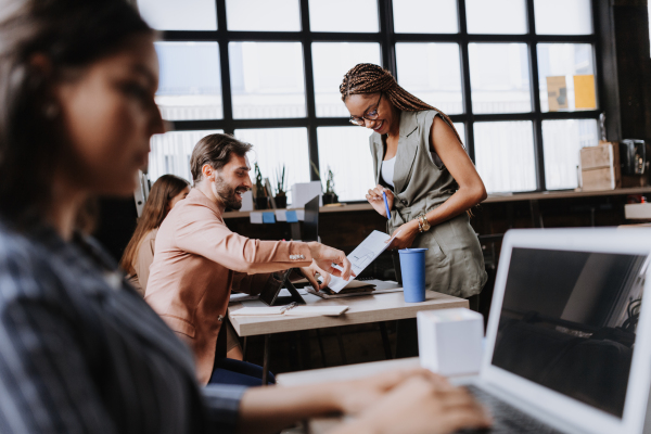 People in coworking space sharing ideas, collaboring, talking about project. Group of freelancers and remote businesspeople working in shared work area. Concept of coworking as modern working arragement. Working remotely from coffee shop.